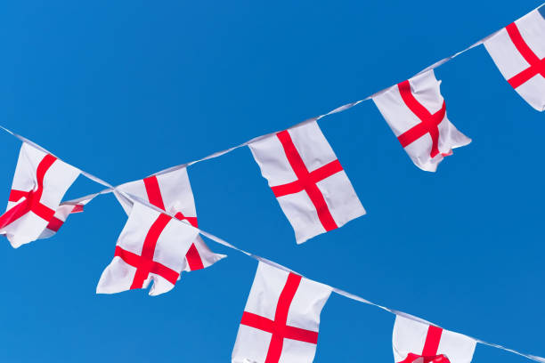 istock Single row of England flags / bunting flying against blue sky. 996966168