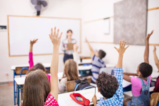 istock School children raising hands in classroom 996966232