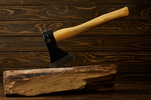 closeup view of sticking axe in log on brown wooden surface