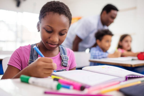 istock Schoolgirl writing in book at desk 996975404