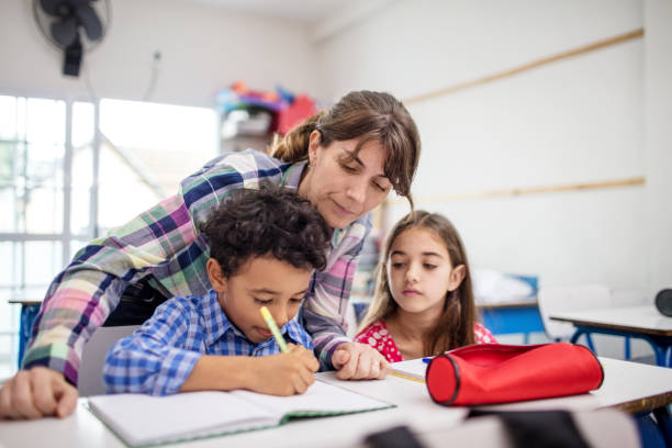 istock Teacher and girl looking at boy writing in book 996976268
