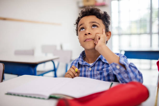 istock Thoughtful boy with book on desk in class 996978960