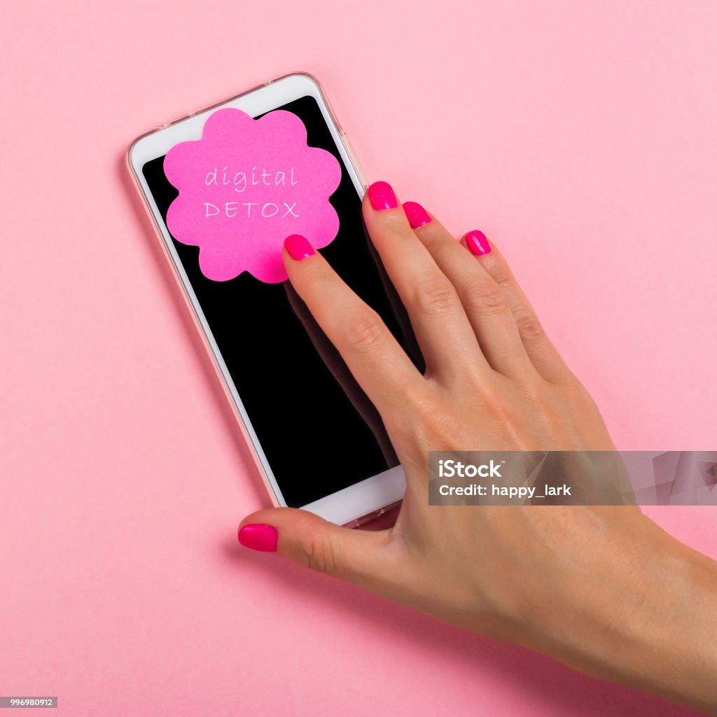 Female hand reaching for cell phone Female hand with pink manicure reaching for cell phone with blank screen. Digital detox concept. Pink background with copy space. Flat lay style Detox Stock Photo