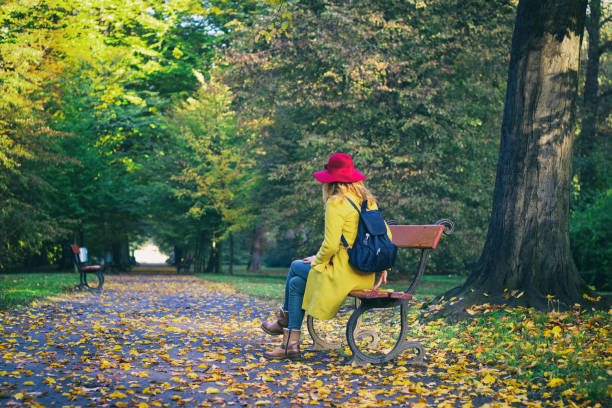 istock Young woman with backpack sitting on a bench in autumn park. 996994212