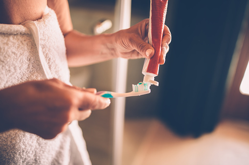 Close-up of senior woman's hands squeezing and applying toothpaste on toothbrush to brush her teeth