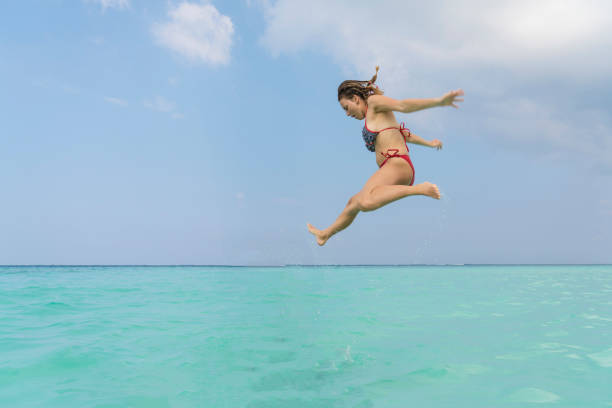 Beautiful young women jumping high up from turquoise sea against clear blue sky in Maldives.