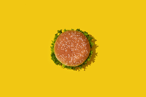 Sabrosa hamburguesa insalubre fresco con salsa de tomate y verduras sobre fondo brillante vibrante amarillo. Vista superior con copia espacio photo