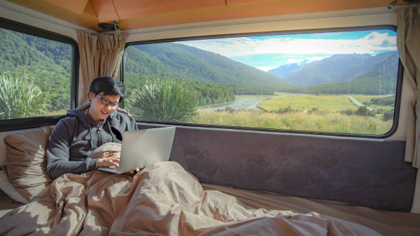 istock Young Asian man working with laptop computer on the bed in camper van with mountain scenic view through the window, digital nomad on road trip concept 997023502