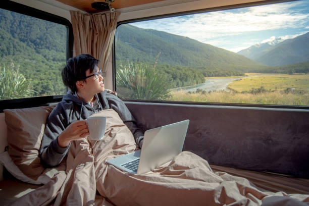 istock Young Asian man drinking hot coffee working with laptop computer on the bed in camper van with mountain scenic view through the window, digital nomad on road trip concept 997023504