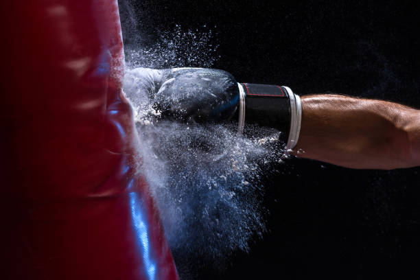 mano ravvicinata del pugile al momento dell'impatto sul sacco da boxe su sfondo nero - lotta sport foto e immagini stock