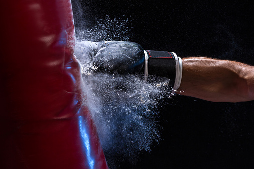 Close-up hand of boxer at the moment of impact on punching bag over black background. Strength and motivation. Studio shot