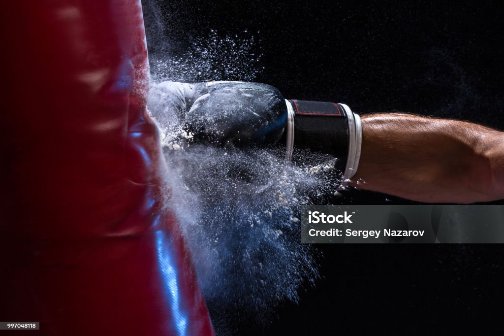 Close-up hand of boxer at the moment of impact on punching bag over black background Close-up hand of boxer at the moment of impact on punching bag over black background. Strength and motivation. Studio shot Boxing - Sport Stock Photo
