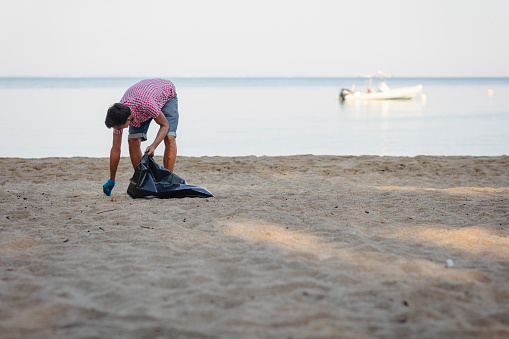 Young man collecting trash on beach early in the morning.