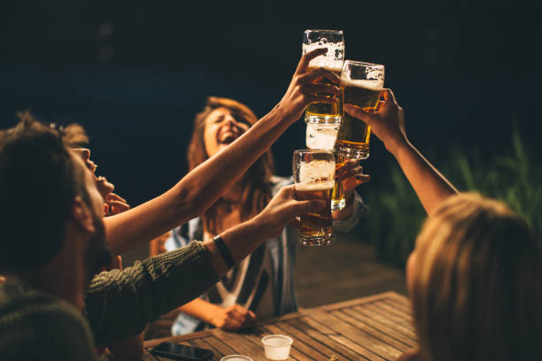 Group of friends drink beer on the terrace and toast during summer night stock photo
