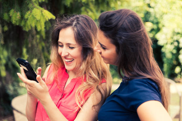 istock Happy female friends using mobile phone in the park. 997082262