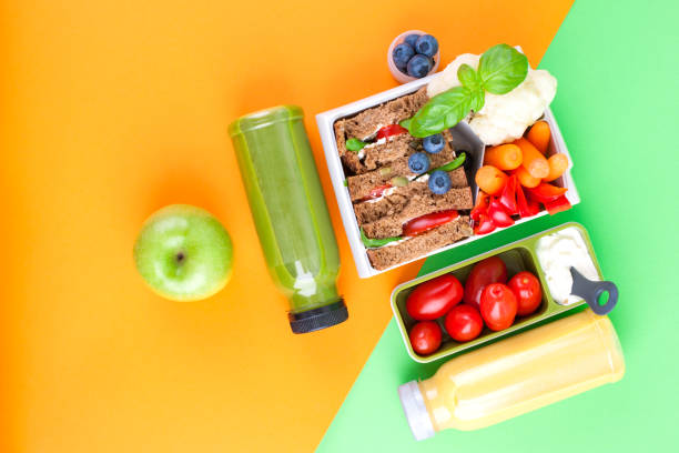 caja de almuerzo con comida sana y de zumo de bayas frescas. pan tostado y manzana. libros para la escuela y fondo verde. comida para llevar. copia espacio. lay flat - lunch box lunch box metal fotografías e imágenes de stock