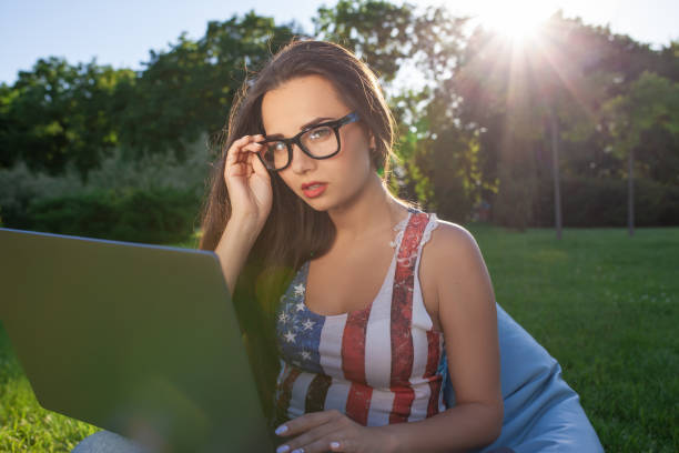 bela jovem sentada no laptop de uso de saco de feijão, enquanto descansava na grama no parque do sol - coffee bean bag human hand - fotografias e filmes do acervo