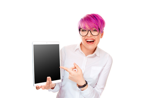 Attractive young excited woman pointing with finger hand at her pad computer standing isolated on white background smiling happy laughing. Millennial model with pink magenta hair.