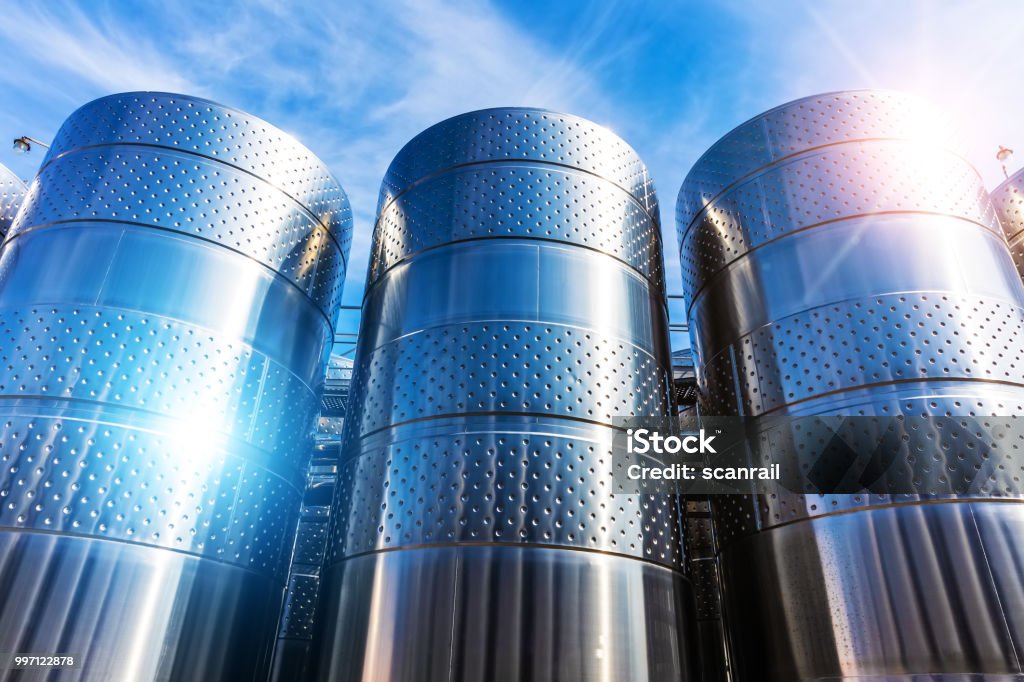 Stainless steel storage tank containers at the chemical plant factory Row of the shiny stainless steel storage tank containers at the chemical plant factory against blue sky with clouds Industry Stock Photo