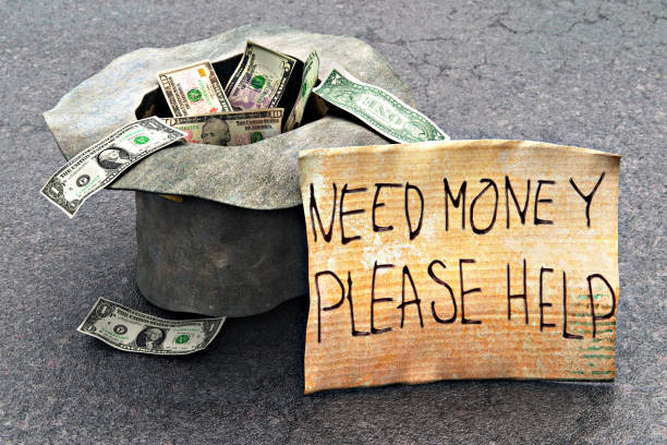Macro view of the homeless poor beggar's hat with dollar money cash banknotes and the help message on the piece of cardboard on the street road asphalt outdoors