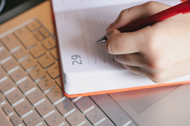 Student writing in the notebook on the computer keyboard stock photo