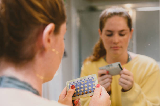 Woman Thinking About Her Health With Birth Control Pills Woman in mirror examining birth control pills. birth control pill stock pictures, royalty-free photos & images