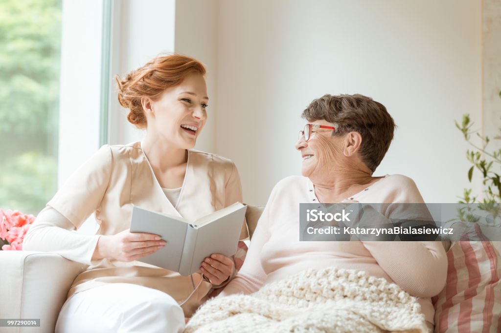 Happy Nurse Reading A Funny Book To Her Elderly Patient In A Private Nursing Home Stock Photo - Download Image Now - iStock Happy Nurse Reading A Funny Book To Her Elderly Patient In A Private Nursing Home Stock Photo - Download Image Now - iStock
