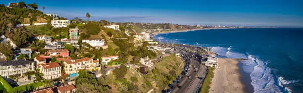 Aerial panorama of the Pacific Coast Highway hugging the beach and curving between the ocean and the town of Malibu, California.