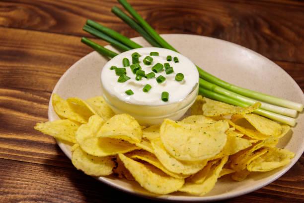 istock Crispy potato chips with green onion and sour cream on wooden table 997340640