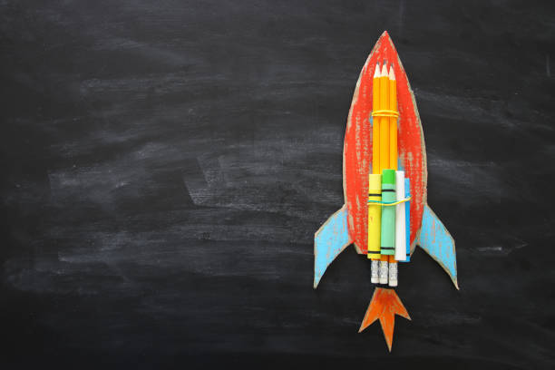 istock Back to school concept. Top view image of handmade cardboard rocket and clouds with pencils over classroom blackboard background 997341568