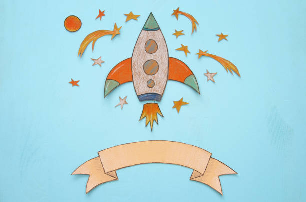 istock Rocket cut from paper and painted over wooden blue background. 997341760