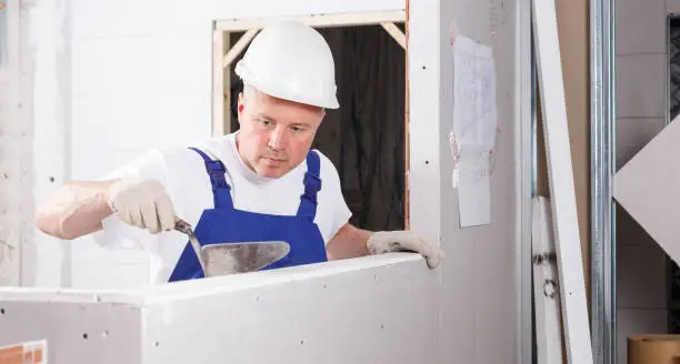 Confident builder filling gaps on drywall element with setting compound inside building under construction