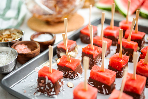 Preparing watermelon appetizers dipped in chocolate and sprinked with sea salt and almonds.
