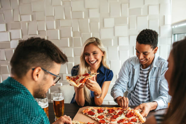 Don't be shy, eat with us! Shot of a group of friends drinking beer and eating pizza in a bar dont eat meat stock pictures, royalty-free photos & images