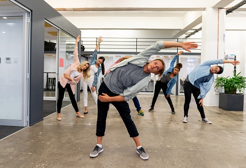 Group of workers on an active break at a creative office stretching and looking happy - healthy lifestyle concepts