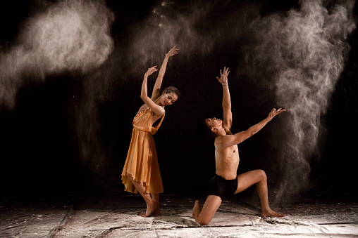 Beautiful couple ballet dancer with white powder explosion over black background