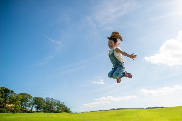 青い空にジャンプの女の子 - 子供時代 ストックフォトと画像