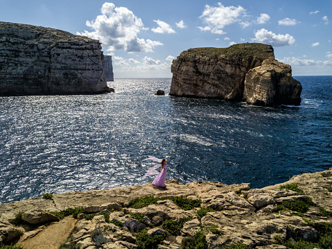 A woman in a wedding dress atop a cliff on the island of Gozo, country of Malta