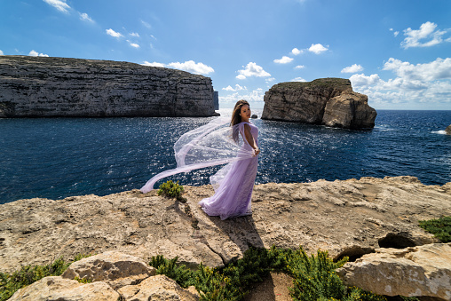 A woman in a wedding dress atop a cliff on the island of Gozo, country of Malta