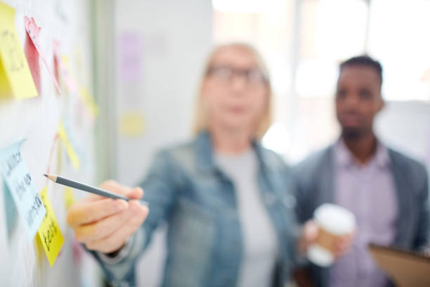 istock Close-up of unrecognizable woman pointing at adhesive note with text while explaining marketing plan to colleague 997398020