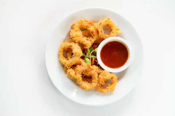Photo of Fried crispy squid rings breaded ( caramari ) with red sauce on white backgruond