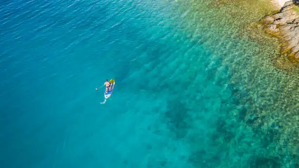 Aerial view of young man riding paddleboard. Paddleboarding is the modern way of transportation and water activity sport.