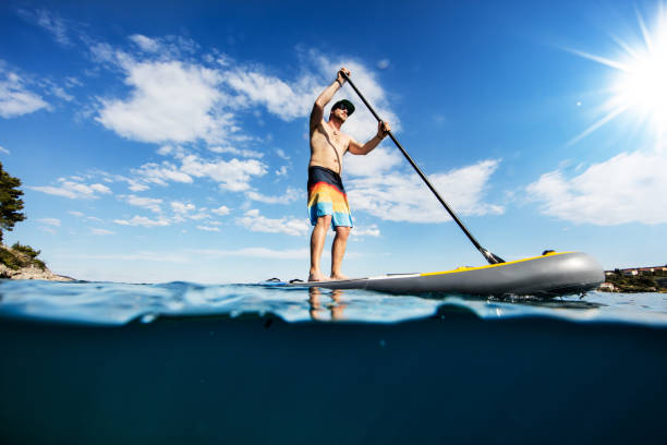 Young man on paddleboard, half under and half above water composition Young man on paddleboard, half under and half above water composition. Paddleboarding is the modern way of transportation and water activity sport. paddleboard surfing oar water sport stock pictures, royalty-free photos & images