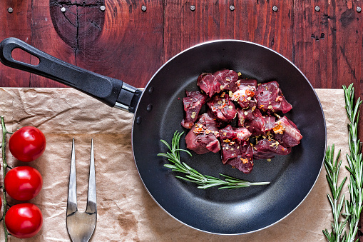 Raw beef in the frying pan, cherry tomatoes, and spices romarinho on wooden background. Italian food. top view, copy space