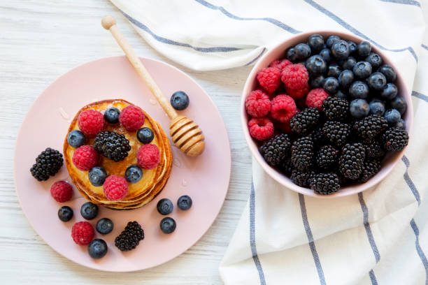 Pancakes with berries and honey on a pink plate, bowl of berries, top view. Closeup.