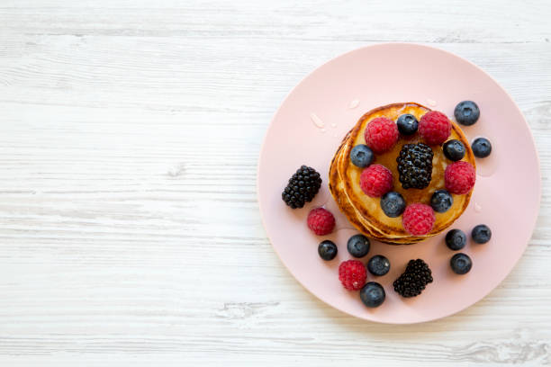 Pancakes with berries and honey on a pink plate, view from above. Copy space.
