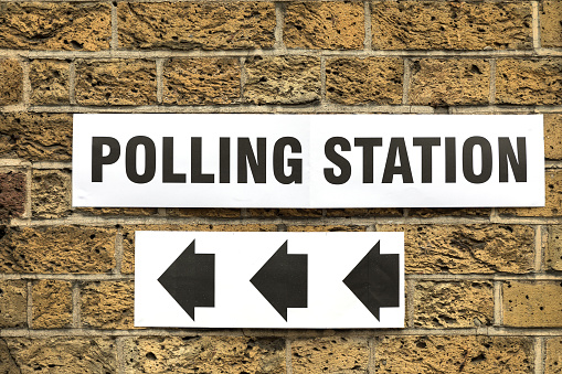 Polling Station sign on yellow brick wall in London, UK, with arrows pointing the way in to vote.
