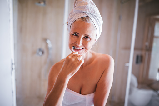 Happy retired mature woman brushing her teeth for fresh smile in the morning