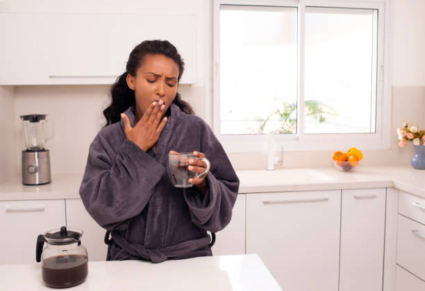 svegliarsi donna bevendo caffè mattutino in cucina. - yawning women drink coffee cup foto e immagini stock