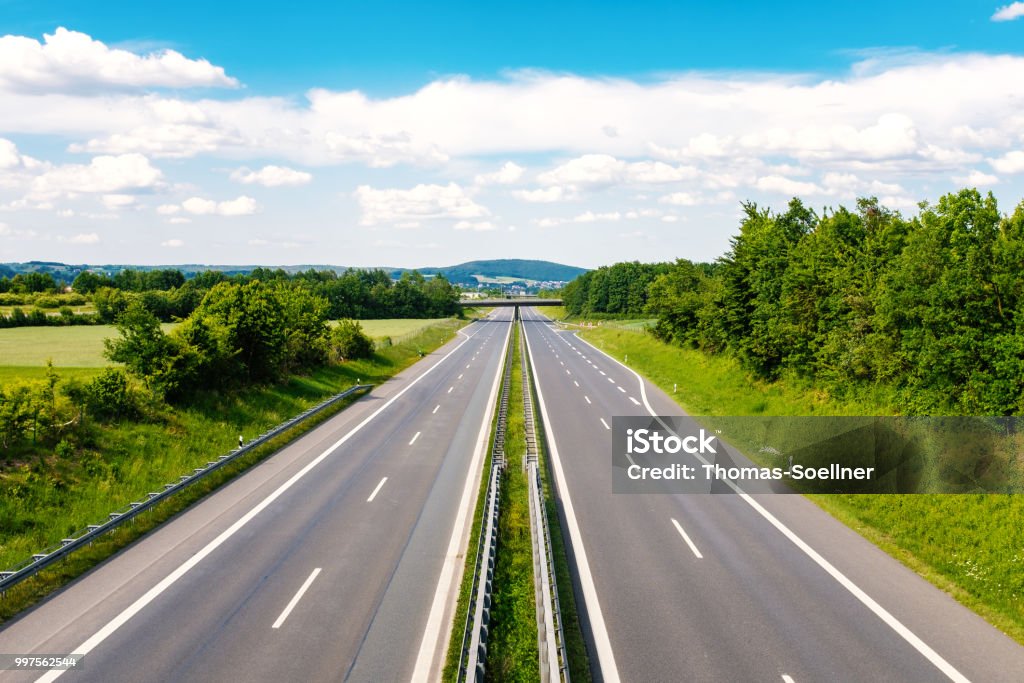 Traffic Empty highway through a green landscape with clouds on a blue sky Highway Stock Photo